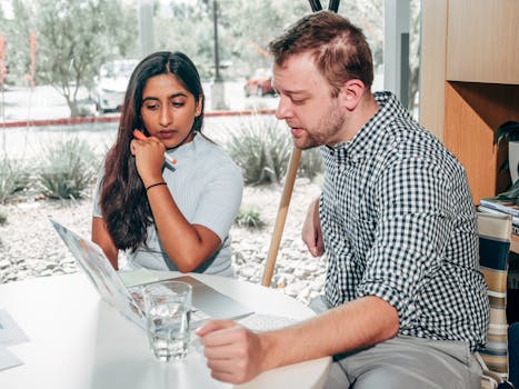 A diverse group of two adults collaborating on a project using a laptop in an office setting.