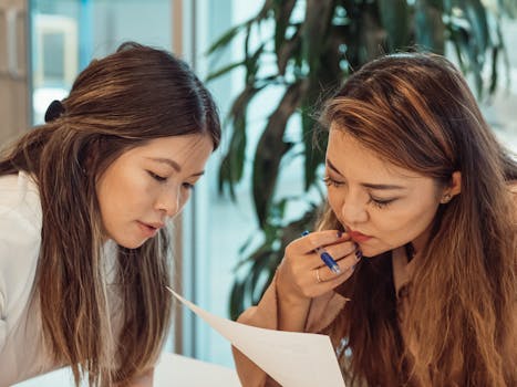 Two women collaborating in an office setting, focusing on documents.